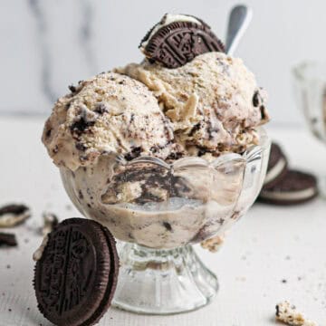 A glass dessert cup filled with rich cookies and cream ice cream, topped and surrounded by crunchy chocolate sandwich cookies.