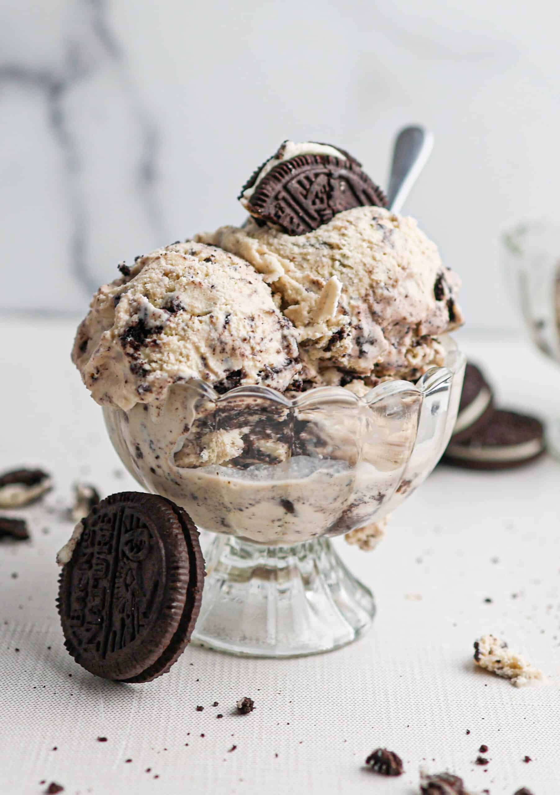A glass dessert cup filled with rich cookies and cream ice cream, topped and surrounded by crunchy chocolate sandwich cookies.