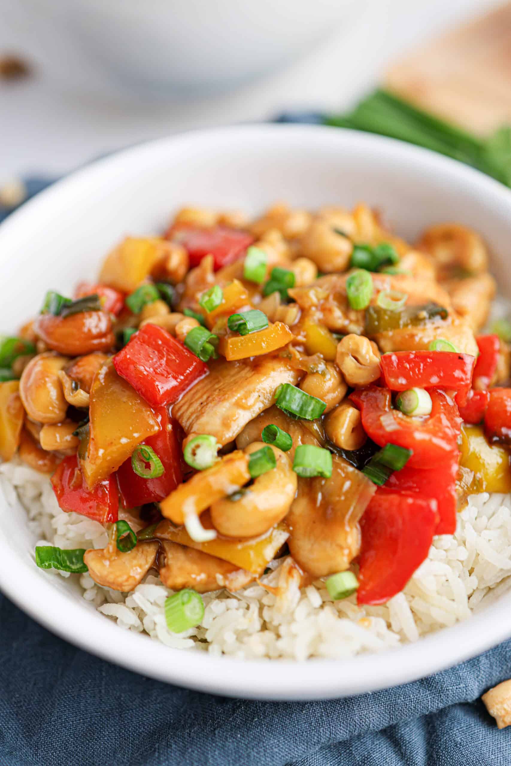 A bowl of rice topped with flavorful cashew chicken, stir-fried with red and yellow bell peppers, crunchy cashews, and chopped green onions.
