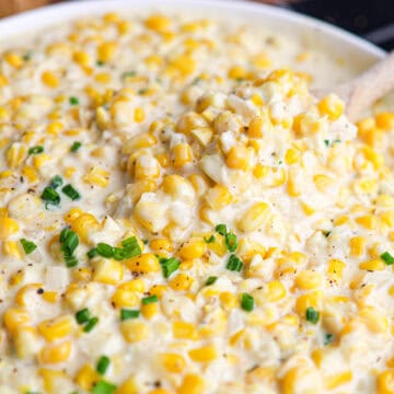 Close-up of creamy corn casserole made with creamed corn, garnished with chopped green herbs, with a spoon scooping some from the dish.
