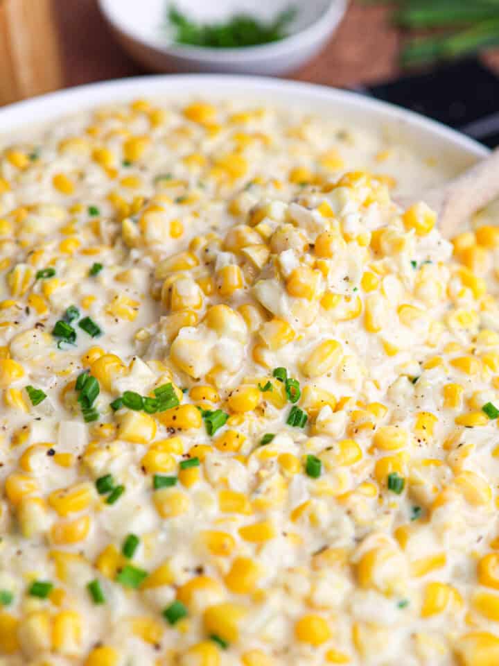 Close-up of creamy corn casserole made with creamed corn, garnished with chopped green herbs, with a spoon scooping some from the dish.