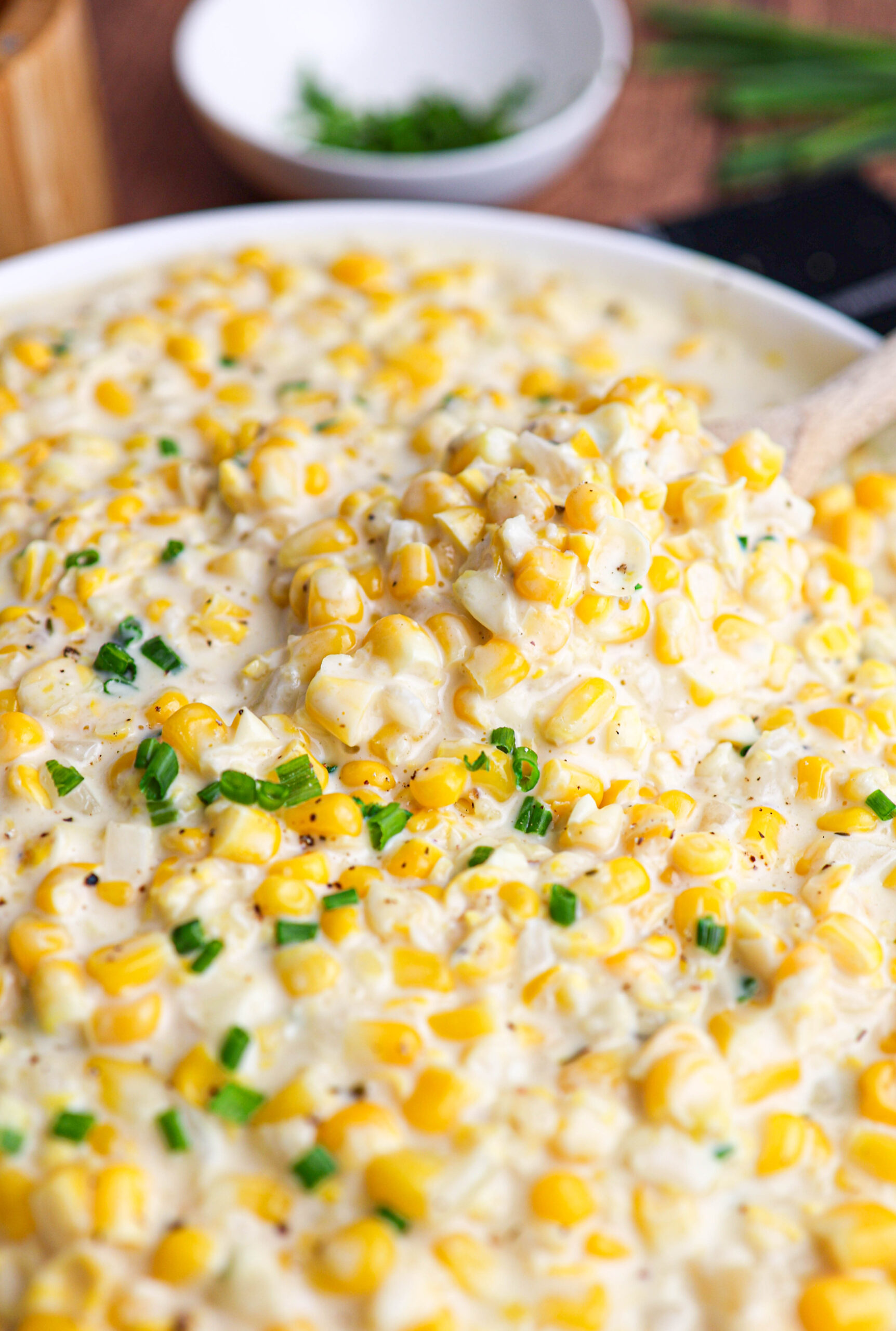 Close-up of creamy corn casserole made with creamed corn, garnished with chopped green herbs, with a spoon scooping some from the dish.