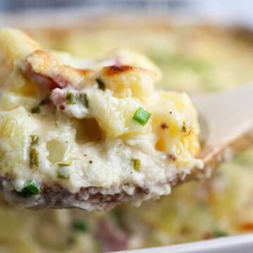 A wooden spoon holds a serving of creamy ham and potato casserole topped with chives.